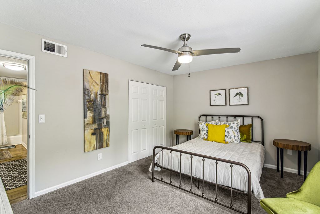 Staged bedroom with carpeted floors, a bed, two nught stands and modern ceiling fan.