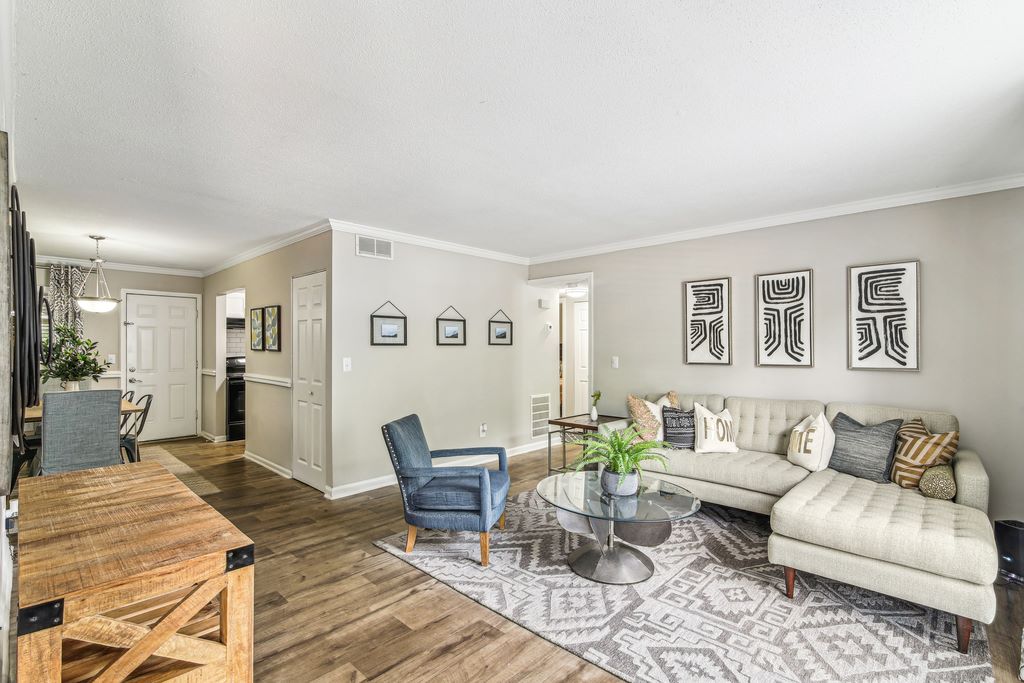 Staged living room with hardwood style flooring, couch, accent table and decorative rug with dining room in background.