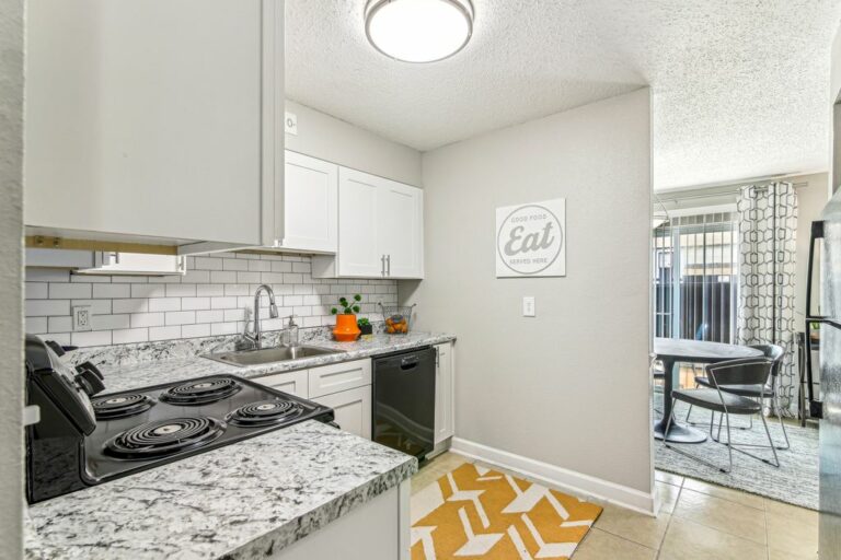 Kitchen with black appliances, granite style counter tops, white shaker cabinets, white subway tile backsplash, and tile flooring.