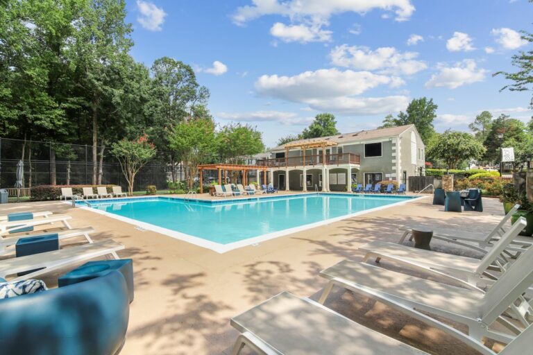 Swimming pool with sundeck and lounge chairs surrounded by native landscaping with leasing office in background.