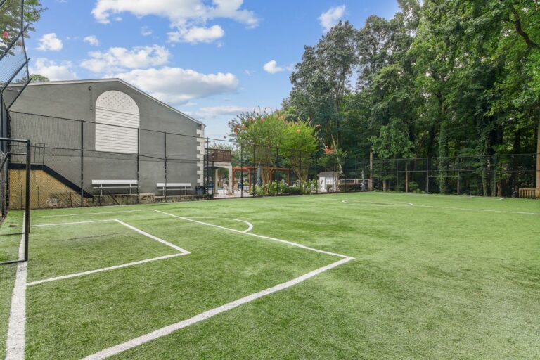 Fenced in turf sports court with pool in background.